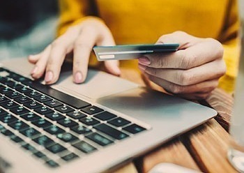 Woman holding card typing on laptop.