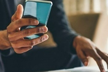 Man holding phone and using laptop.