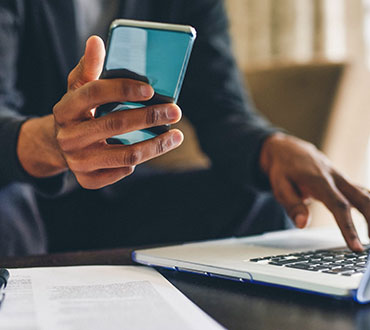 Man holding phone and using laptop.