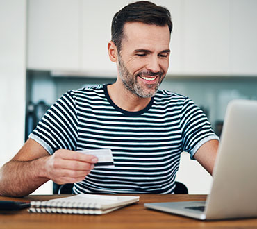 Man holding card using laptop.