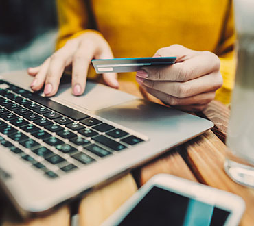 Woman holding card typing on laptop.